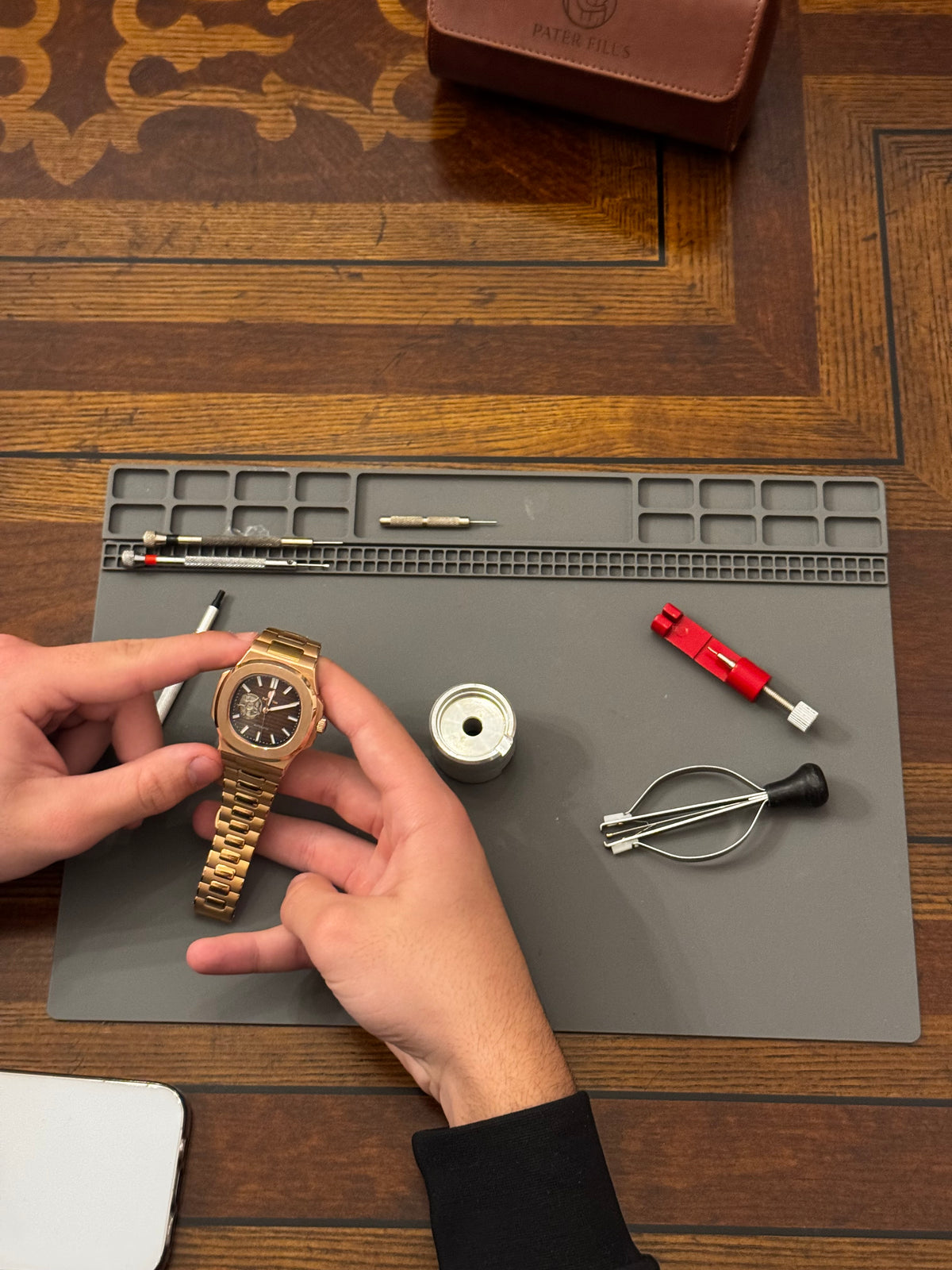A watchmaker's hands working on a gold Pater Filus watch at the bench